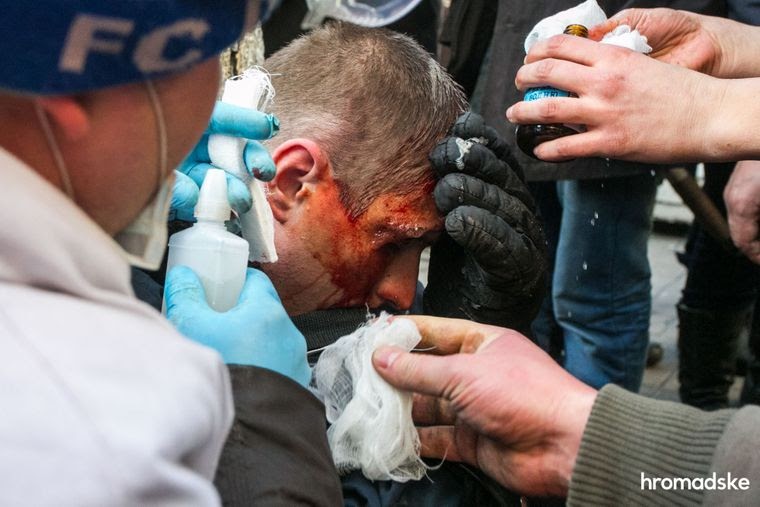 Протестующие оказывают помощь раненому силовику, 18 февраля 2014 года
