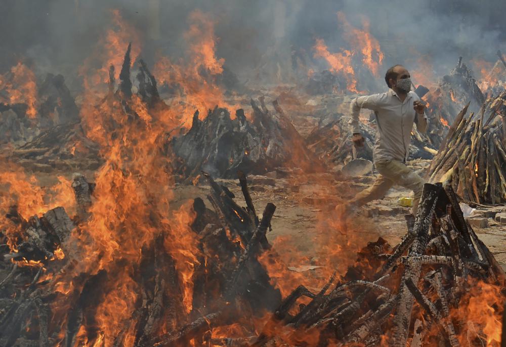FILE - In this April 29, 2021, file photo, a man runs to escape heat emitting from the multiple funeral pyres of COVID-19 victims at a crematorium in the outskirts of New Delhi, India. India’s excess deaths during the pandemic could be a staggering 10 times the official COVID-19 toll, likely making it modern India’s worst human tragedy, according to the most comprehensive research yet on the ravages of the virus in the south Asian country. (AP Photo/Amit Sharma, File) dqxikeidqxitkant