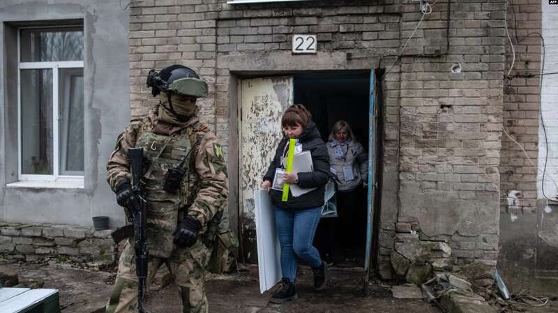 Российский военнослужащий сопровождает членов избирательного участка на так называемых выборах президента России, 17 марта 2024 года. dqxikeidqxitkant