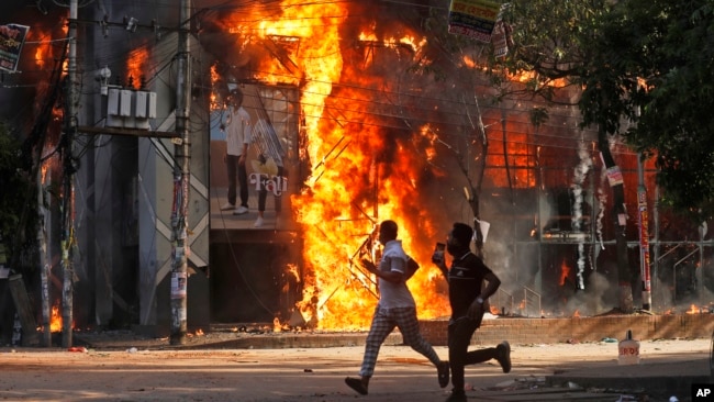 Мужчины пробегают мимо торгового центра, который подожгли протестующие во время митинга против премьер-министра Шейх Хасины и ее правительства, Дакка, 4 августа 2024 года